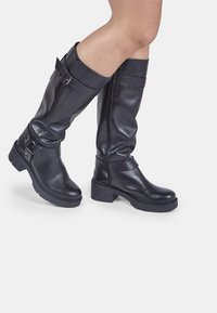 Botas de cuero negro altas hasta la rodilla con suela gruesa, que cuentan con dos hebillas ajustables y un acabado suave.