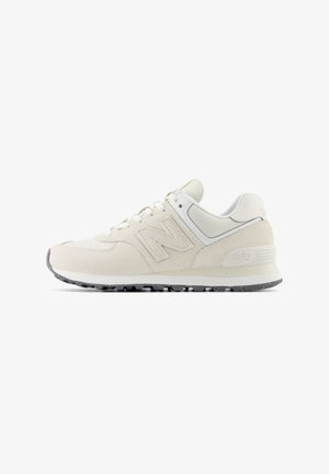 White suede sneaker with textured paneling, lace-up design, prominent 'N' logo, and gray rubber sole. Features smooth accents and subtle patterns.