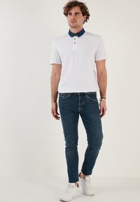 Fehér, rövid ujjú pólóing, denimszínű gallérral és három gombos pánttal, sötétkék slim fit farmernadrággal és fehér sportcipővel párosítva.