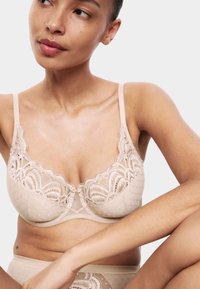 Beige kanten beha met een polkadotpatroon, gegolfde randen en een transparant gedeelte in het midden. Verstelbare bandjes en een delicate haaksluiting.