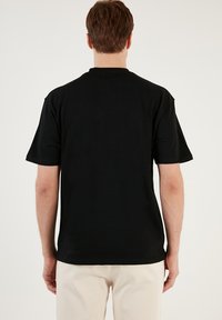 Tricou din bumbac negru cu mâneci scurte, guler rotund și croială dreaptă. Textură netedă și design minimal, fără logo-uri sau modele.