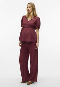 Graviditetsoutfit med en djup bordeauxfärgad texturerad inlindad topp med puffärmar och vida byxor, båda i ett lätt material.