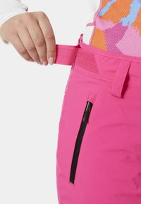 Růžové sněhové kalhoty s texturovaným povrchem, vybavené černou zipovou kapsou a nastavitelným páskem v pase.