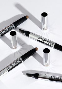 Four Maybelline Tattoo Brow Lift Stick tools with caps removed, showing spoolie brush and brow pencil tips on white surface.
