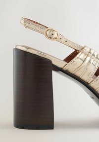 Gold metallic high-heeled sandal with a thick dark wooden block heel and adjustable ankle strap with a small gold buckle.