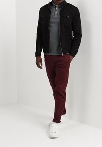 Black zip-up jacket over a gray polo, paired with burgundy pants and white sneakers. Jacket features two front pockets.