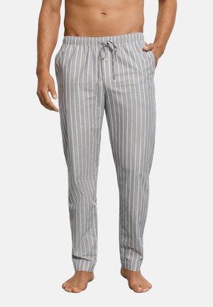 Mand iført grå og hvide pyjamasbukser med lodrette striber og snoretræk, stående barfodet med den ene hånd i lommen.