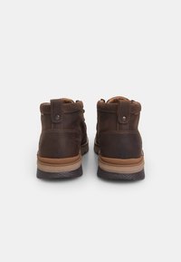 Bottines en cuir marron avec une texture lisse, des coutures contrastantes, un bout rond et des semelles en caoutchouc. Présente des accents en daim et des boutons-pression.