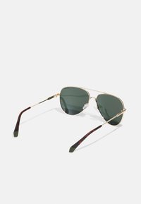 Ochelari de soare aviator din metal aurit cu lentile verzi. Temele au un model de scoică întunecată și accente verzi din cauciuc aproape de vârfuri.