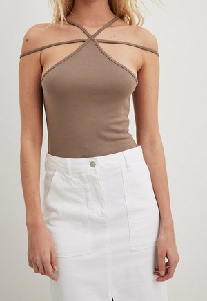 Nainen pukeutunut tummanharmaaseen, ristikkäisiin olkaimiin olevaan hihattomaan toppiin, jonka kanssa on yhdistetty korkea vyötäröinen valkoinen hame, jossa on etutaskut ja napitus.