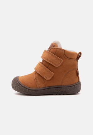 Bottine marron pour tout-petit avec double bride velcro, doublure en fourrure, semelle texturée et languette de traction au talon, vue de profil sur fond blanc.