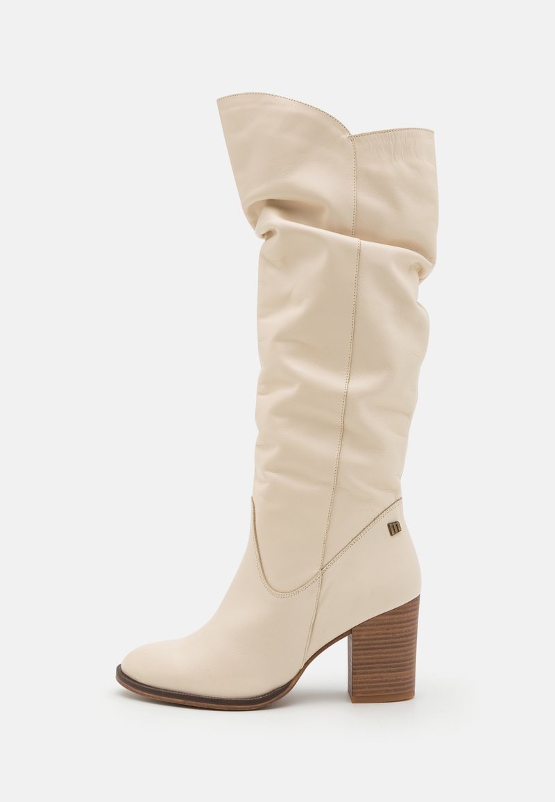 Beige läder knähöga stövlar med en slouchy design, spetstopp och en staplad brun klack. Innehåller subtil sömnad och varumärkesdetaljer.