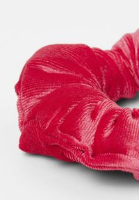 Červená sametová gumička do vlasů s texturovaným, žebrovaným povrchem a nařaseným designem, vykazující měkkost a pružnost látky.