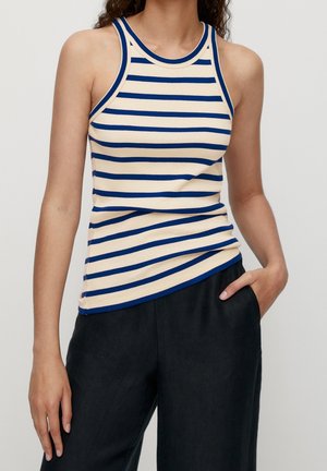 Top sans manches rayé en crème et bleu, avec un col rond et une silhouette ajustée. Porté avec un pantalon sombre, texture lisse.