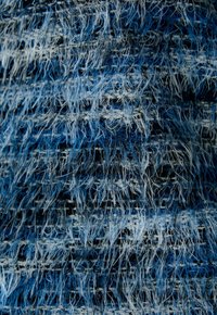 Strukturiertes Gewebe mit einem ausgefransten Finish in verschiedenen Blau- und Weißtönen. Es verfügt über ein geschichtetes, gewebtes Aussehen mit sichtbaren Fasern.