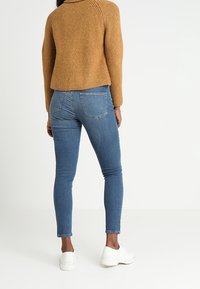 Úzké světle modré džíny s klasickým designem, doplněné strukturální hořčicovým svetr. Bílé tenisky dokončují celý outfit.