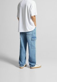 Vit oversized t-shirt, ljusblå cargojeans med sidofickor, avslappnad passform, och vita sneakers med en beige sula.