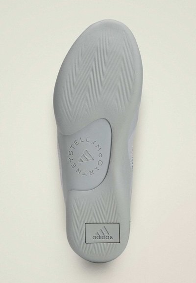 Semelle d'une basket Adidas gris clair avec un motif de crampons en zigzag et un logo circulaire Stella McCartney près de la voûte plantaire.