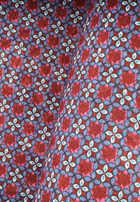 Tkanina z wzorem składającym się z okręgów w kolorze białym, niebieskim i różowym na głębokim czerwonym tle; materiał ma teksturowany wygląd.