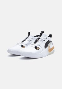 White athletic shoes with a textured upper, black accents, gold detailing, and a cushioned sole. Features a modern design and adjustable straps.