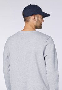 Hellgrauer Sweatshirt mit runder Ausschnitt und langen Ärmeln, kombiniert mit einer marineblauen Baseballmütze, die eine glatte Stoffstruktur zeigt.
