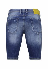 Denim shorts, donkerblauwe wassing, middellang met opgerolde manchetten. Beschikt over twee achterzakken en een gele merkembleem op de tailleband.