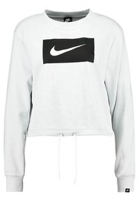 Zkrácená, světle šedá mikina vyrobená z měkké tkaniny. Na přední straně se nachází výrazné černé logo Nike a nastavitelné stahovací šňůrky na lemu.