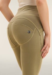 Leggings verdi oliva a vita alta realizzati in materiale elasticizzato; presentano cuciture definite, tasche sagomate e un piccolo etichetta con logo.