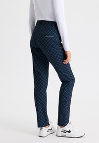 Pantalones azul marino con un patrón de diamantes en líneas azul claro, con un diseño ajustado y un logo en el bolsillo trasero, combinados con zapatillas blancas.