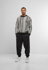 Schwarzer und weißer gemusterter Pullover mit langen Ärmeln, gerippten Bündchen und Saum. Kombiniert mit lockeren schwarzen Jogginghosen und weißen Turnschuhen.