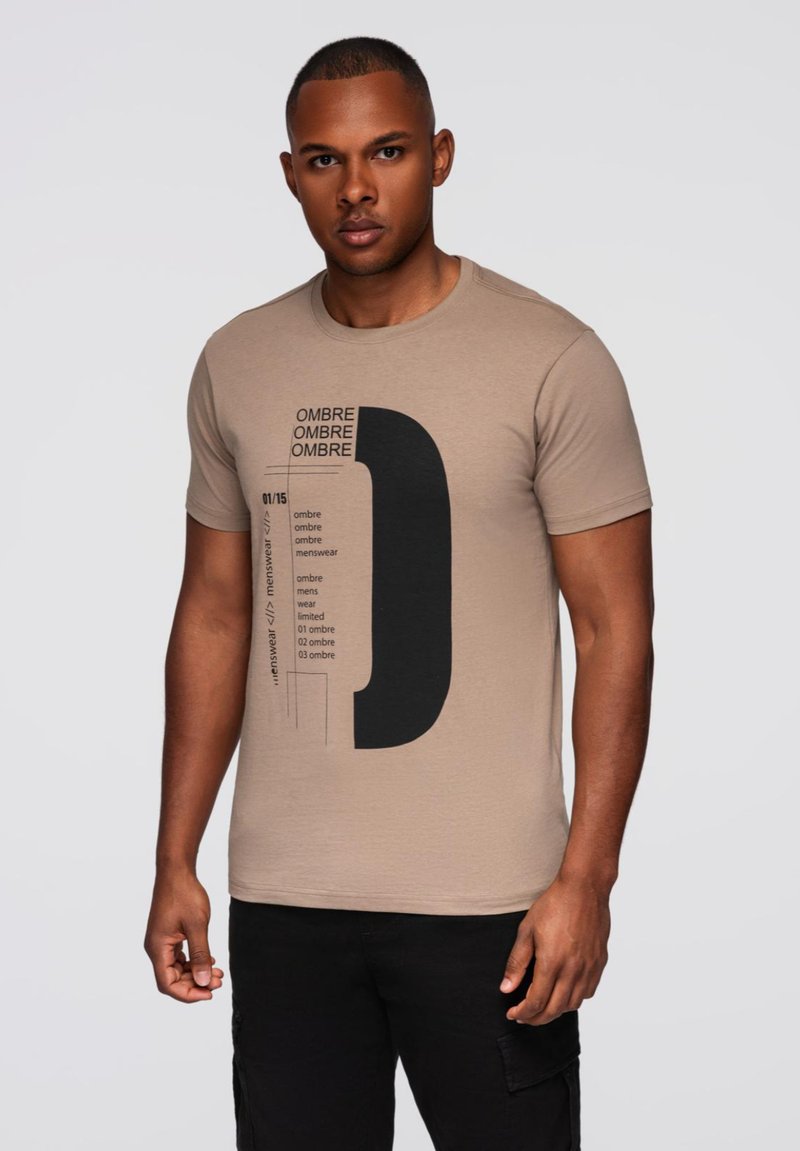 Beige puuvillapaita, jossa on suuri musta graafinen kuvasto tekstillä. Lyhyet hihat, pyöreä kaula-aukko, sileä pinta ja normaali istuvuus.