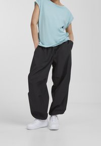 Light blue short-sleeve t-shirt, black loose-fit trousers, and white sneakers, with pockets and hem zippers on pants. Smooth fabric texture.