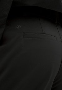 Detailný záber čiernych športových nohavíc s vreckom na zadnej strane a malým logom Lululemon blízko pásu.
