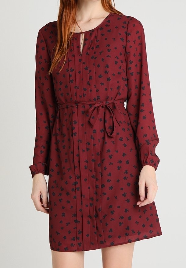 Robe bordeaux à manches longues, avec un col rond et un imprimé floral noir. Détail de ceinture à la taille et tissu froncé au niveau des poignets.