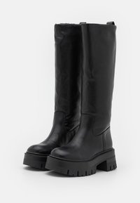 Stivali neri in pelle alti fino al ginocchio con superficie liscia, punta tonda e suola in gomma spessa con profonde scanalature per una buona aderenza.