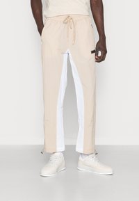 Beiga och vita byxor i ankellängd med elastisk midja och dragsko. Har sidofickor, en logotypspatch och en lätt, slät textur.