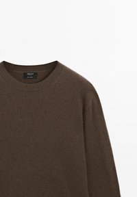 Pull en tricot marron avec un col rond, présentant une texture douce et des détails de poignets côtelés. Étiquette visible à l'intérieur du col.
