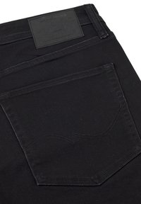 Black denim jeans with a textured surface, featuring a visible rear pocket with stitching details and a branded leather patch at the waistband.