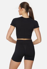 Set atletico nero composto da un crop top aderente con maniche corte e pantaloni corti a vita alta. Tessuto liscio ed elastico con un design elegante.