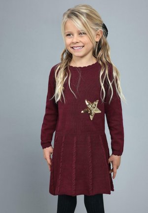 Bordowa dzianinowa sukienka z długimi rękawami i falbaniastym dekoltem. Ozdobiona złotą cekinową gwiazdką oraz teksturowanym detalem w warkocz na spódnicy.