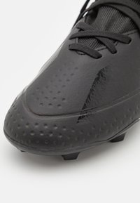 Černý fotbalový kopač s hladkým, lesklým svrškem s texturovaným povrchem a malými kruhovými vměstky, zaoblenou špičkou a zavazováním na tkaničky.