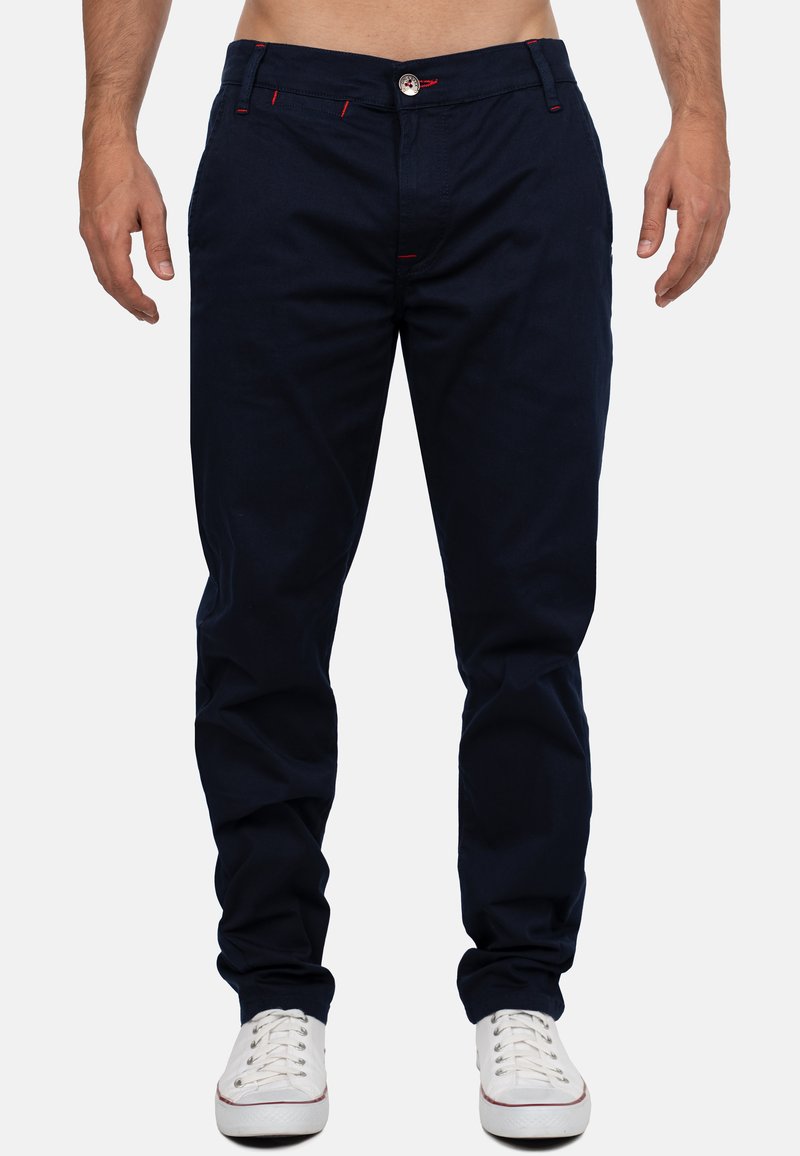 Chino in cotone blu navy con vestibilità dritta, con dettagli di cucitura rossa e chiusura con bottone. Abbinati a sneakers bianche.