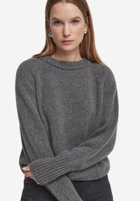 Maglione grigio lavorato a maglia con scollo a girocollo a coste, maniche raglan e tessuto strutturato. Presenta maniche lunghe aderenti e una vestibilità comoda.