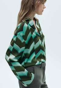 Camicia a maniche lunghe con un motivo a zigzag verde in diverse tonalità di verde e blu. Tessuto morbido, vestibilità rilassata e design con colletto.