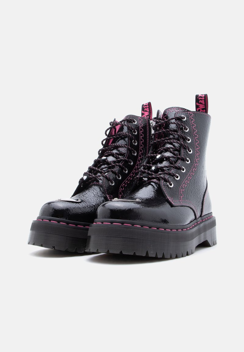 Glanzende zwarte plateauboots met dikke zolen, roze stiksels, zwarte veters met witte hart- en sterbedeltjes, en roze trekbandjes met tekst.