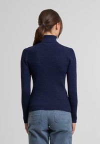 Granatowy sweter z golfem o prążkowanej strukturze, dopasowany do sylwetki. Długie rękawy i wysoki kołnierz. Noszony z jasnoniebieskimi spodniami cargo.