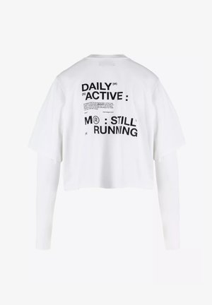 Witte cropped t-shirt met korte mouwen, met op de achterkant zwarte tekst: "DAILY ACTIVE M® STILL RUNNING." Gemaakt van katoen, in een ontspannen pasvorm.