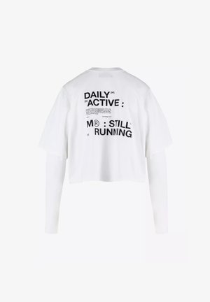 Biała, skrócona koszulka T-shirt z krótkim rękawem, z czarnym tekstem na plecach: "DAILY ACTIVE M® STILL RUNNING." Wykonana z bawełny, luźny krój.