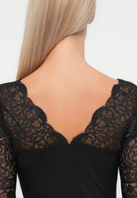 Black garment with intricate lace accents on the shoulders and neckline, featuring a v-shaped back design. Soft texture and fitted shape.