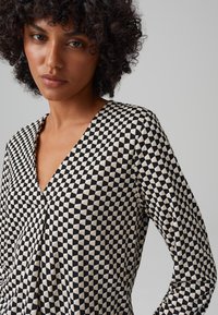 Schwarz-weißer geometrisch gemusterter Oberteil mit V-Ausschnitt, langen Ärmeln und einer weichen Textur, der ein markantes dreieckiges Design aufweist.